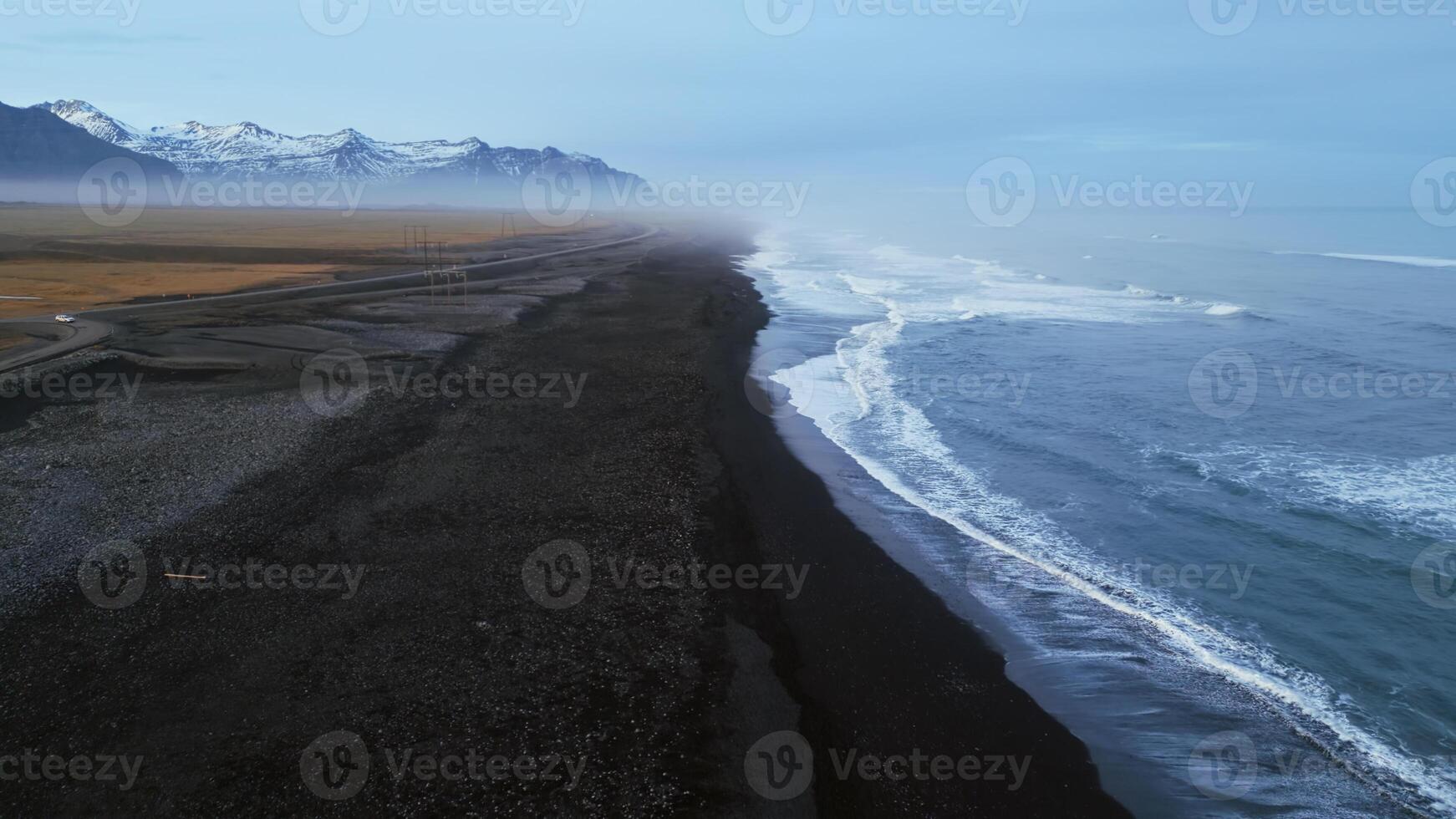 Icelandic black sand beach drone shot, beautiful coastline with waves crashing on atlantic shore. Nordic landscape with snowy mountains and black sand on beaches, scenic route. Slow motion. photo