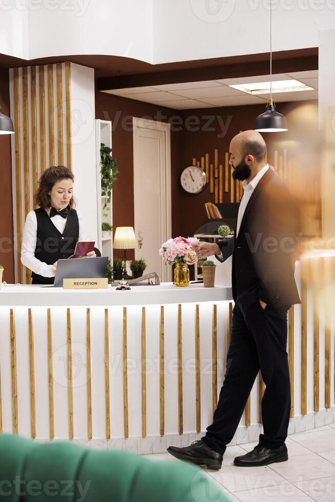 Businessman with passport id papers preparing to do check in for room reservation, reviewing documents at front desk reception. Client travelling for work to attend official meetings. photo