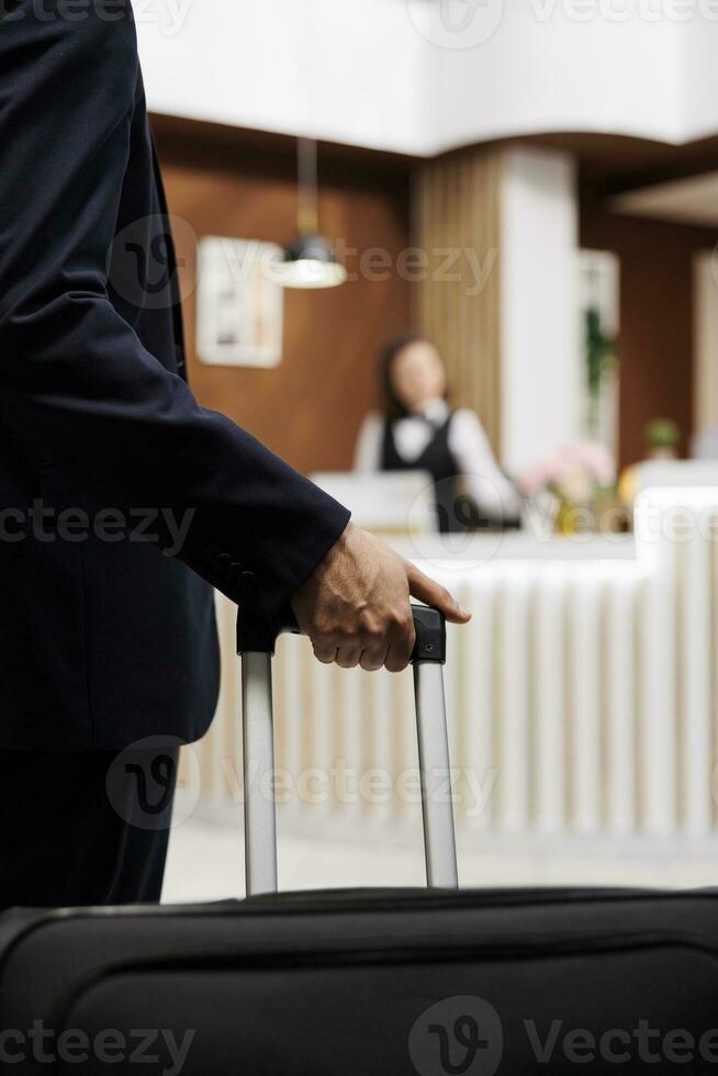 Hotel guest entering reception with luggage, travelling abroad to attend important business meetings. Entrepreneur approaching front desk for check in, booking accommodation. Close up. photo