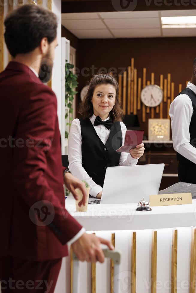 Employee checking guest passport to validate online booking reservation, man travelling for work. Front desk staff verifying identification documents and providing excellent concierge services. photo