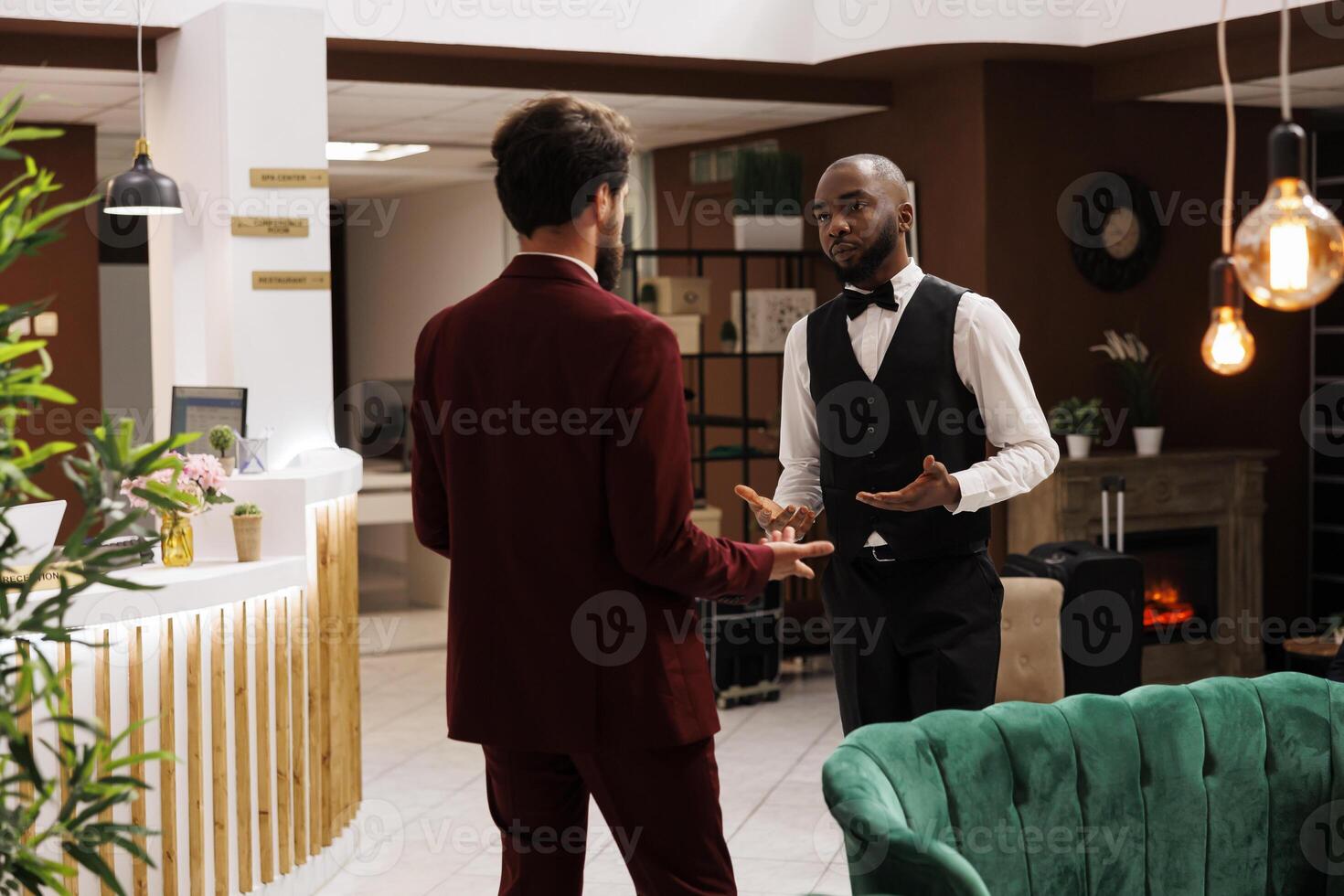 Guest and bellboy discussing in lobby, asking about local recommendations while he is visiting on business trip. White collar worker being greeted by bellhop at hotel, luxury services. photo