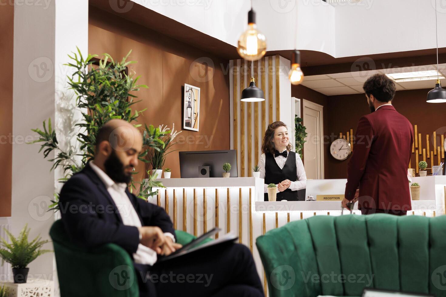 Hotel staff greeting businessman travelling on work trip, friendly receptionist ensuring easy check in process and pleasant stay at luxury resort. Young man in suit meeting employee at front desk. photo