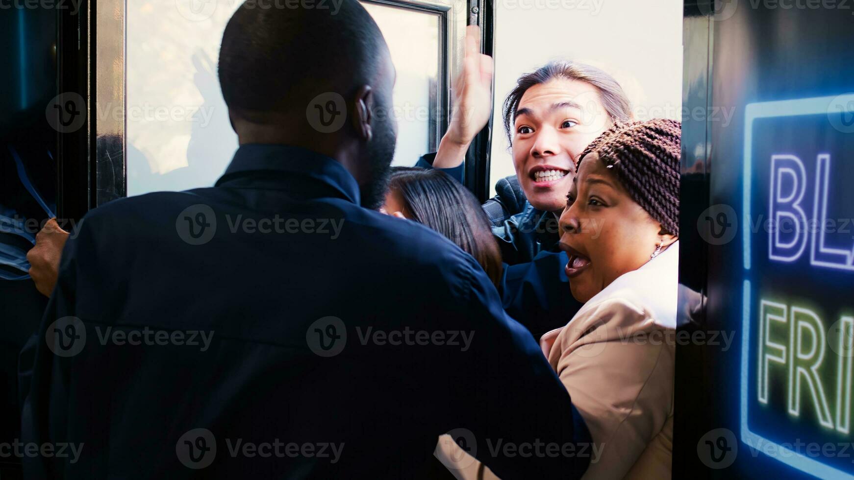 Out of control crowd of mad people breaking into shopping mall during black friday event, knocking agent to hurry inside clothing store and benefit from best deals and promotions. photo