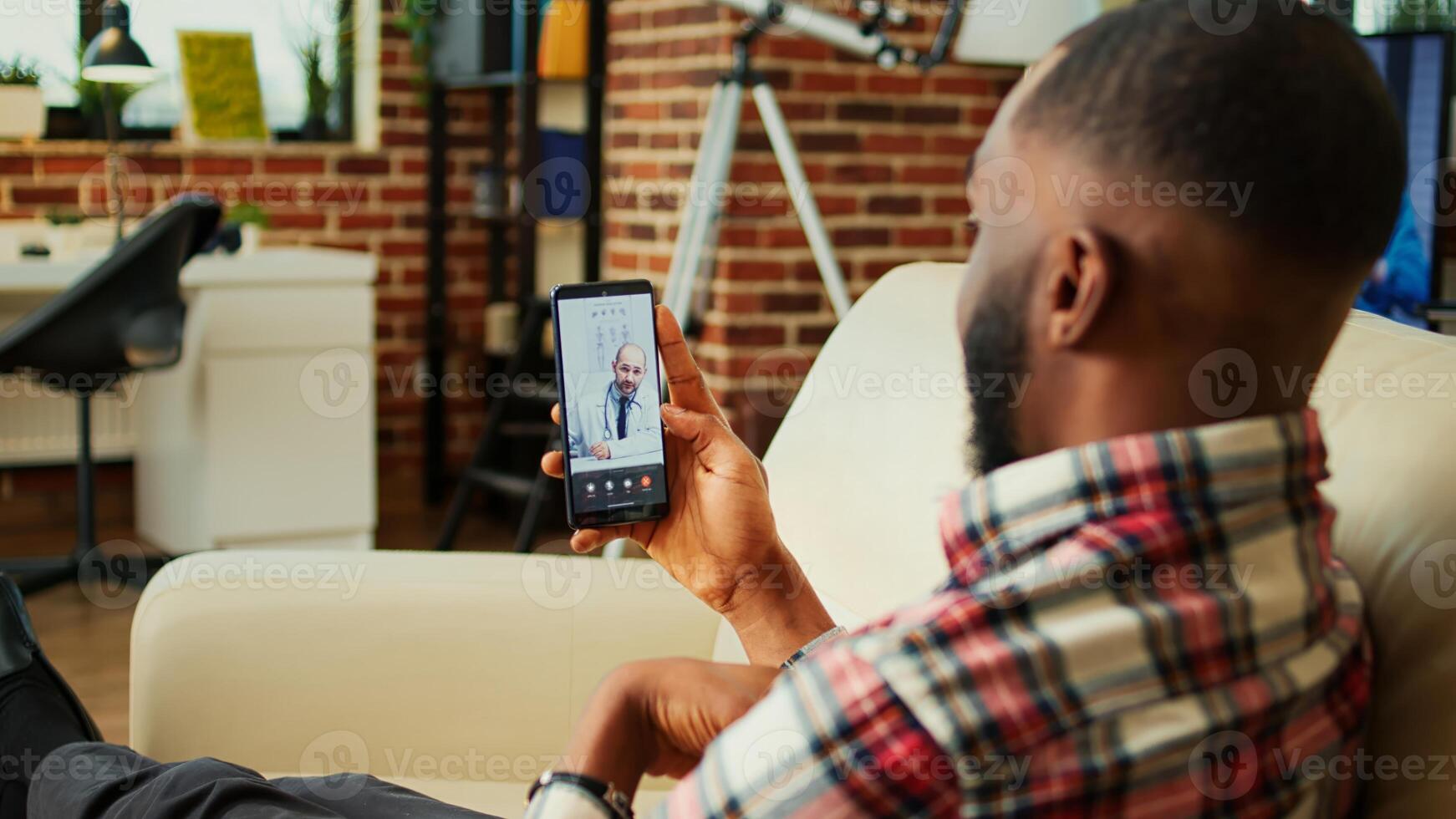 Patient lying on couch remotely discussing treatment plan with doctor during online video call meeting after medical checkup. Man receiving prescription from general practitioner in telemedicine call photo