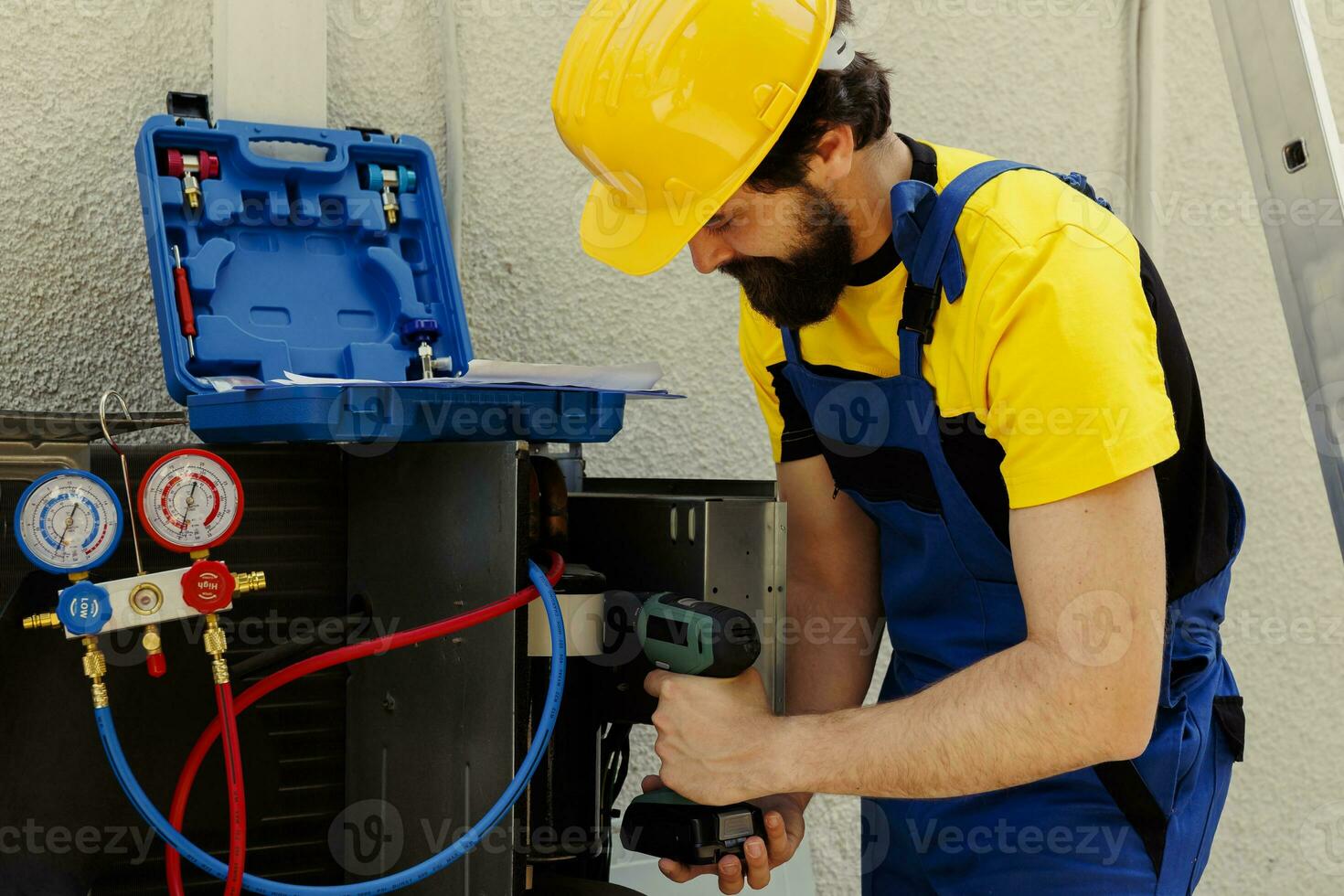 Knowledgeable professional using pneumatic drill to fix system electrical problems caused by defective capacitor. Seasoned mechanic working on defective air conditioner photo