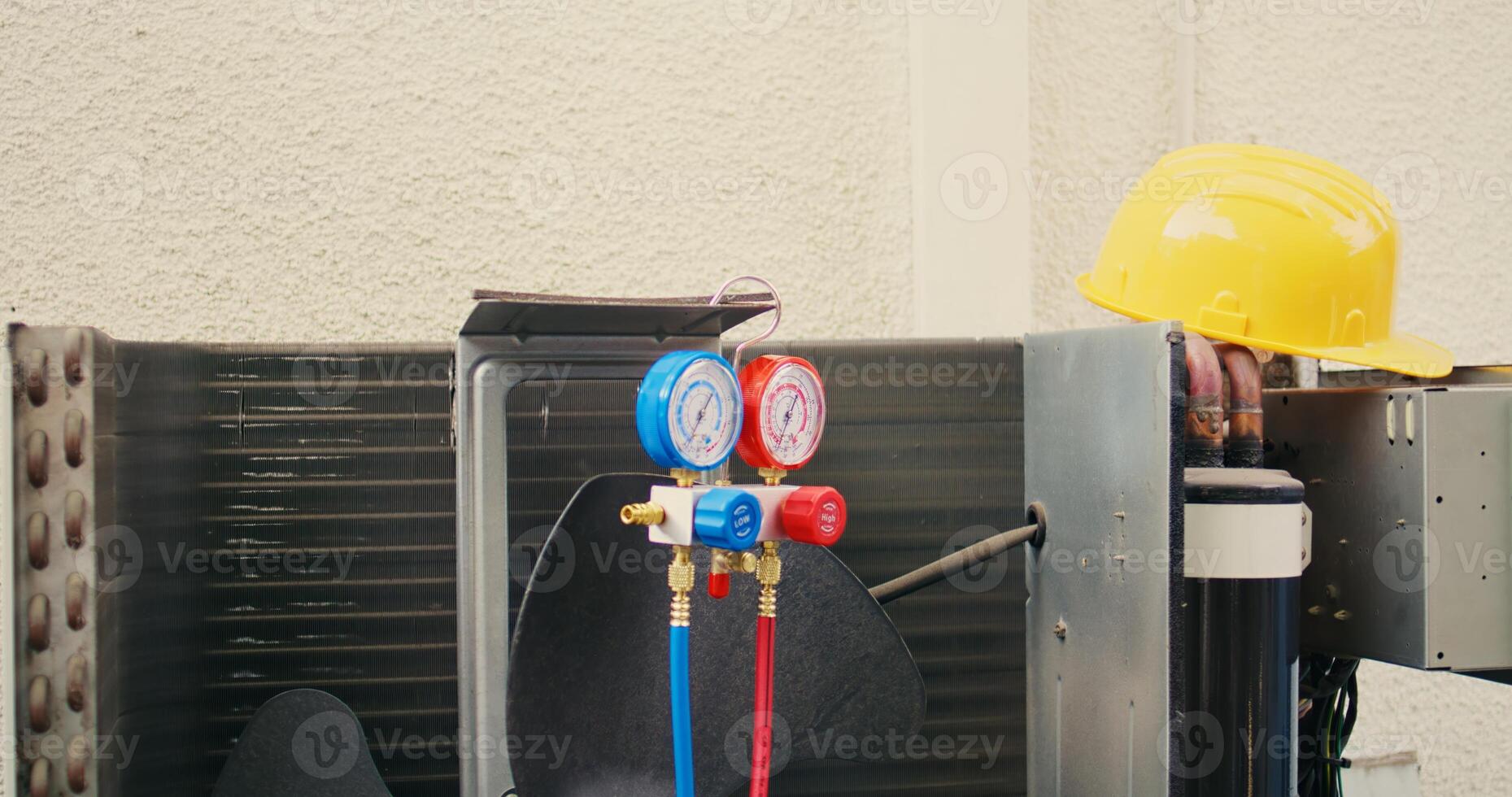 Close up of safety hardhat and pressure measurement device used for checking HVAC system refrigerant in need of maintenance. Set of freon levels benchmarking tool mounted on air conditioner photo