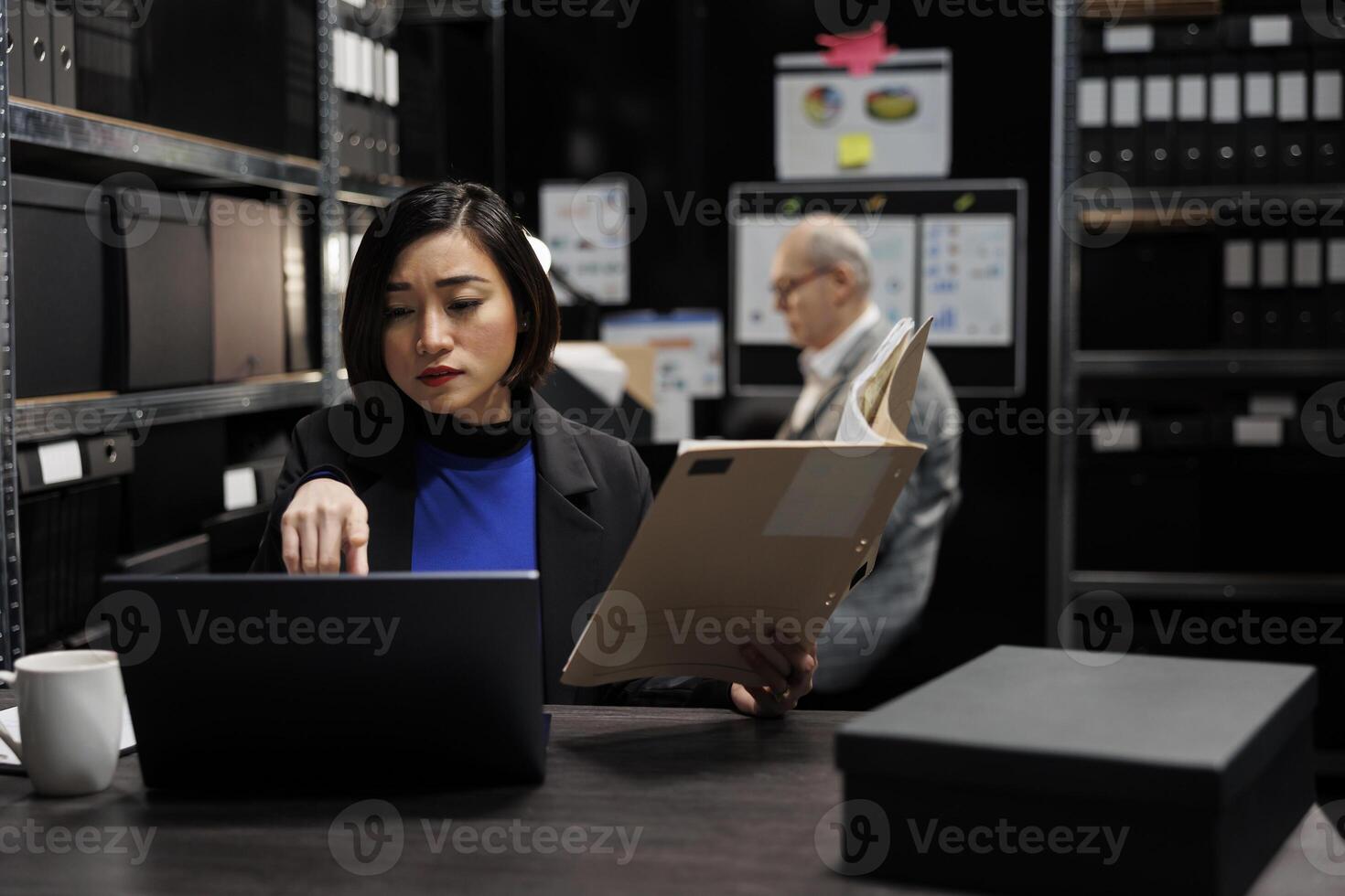 Asian manager accountant checking annual profit revenue paperwork before business consulting meeting. Bureaucratic workplace filled with flowcharts and file folders on shelves photo