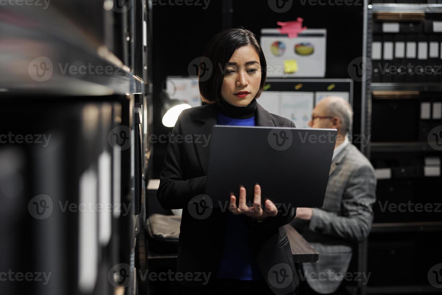 Accounting businesswoman in file cabinet office checking bookkeeping analytical data on laptop. Administration asian executive in business company archival room filled with paperwork folders photo