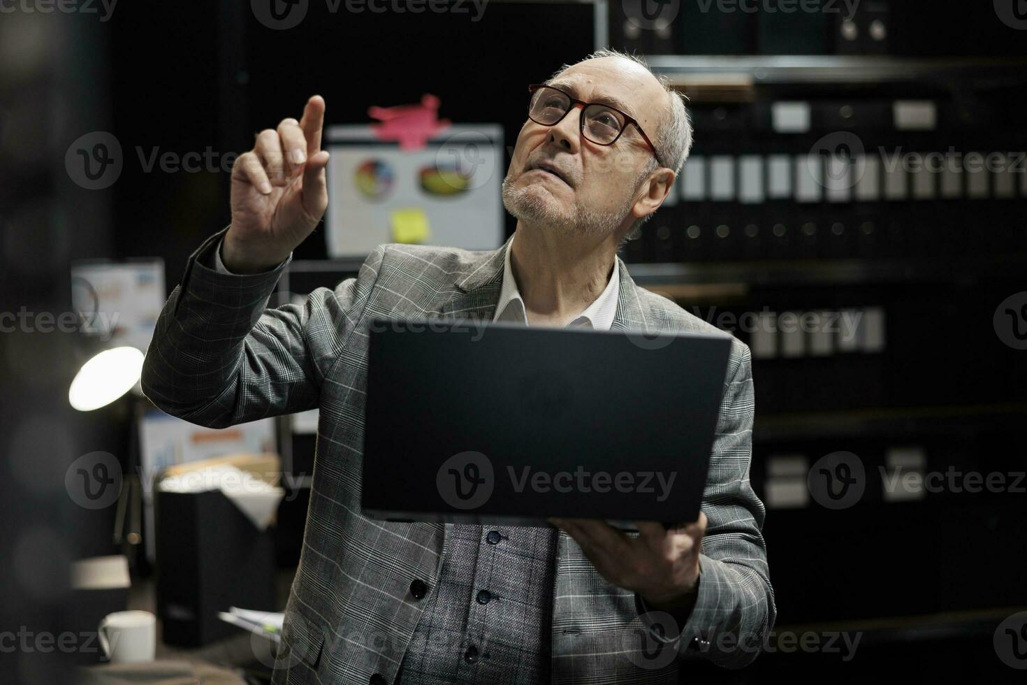 Professional elderly accountant looking for accountancy bureaucratic analytical data paperwork on file cabinet shelves. Senior businessman in storage repository office room photo