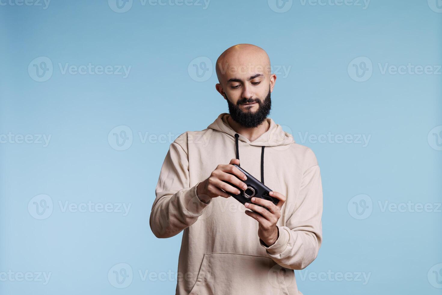 Concentrated arab man playing online game on smartphone. Young carefree bald bearded gamer enjoying leisure time and having fun while using videogame application on mobile phone photo