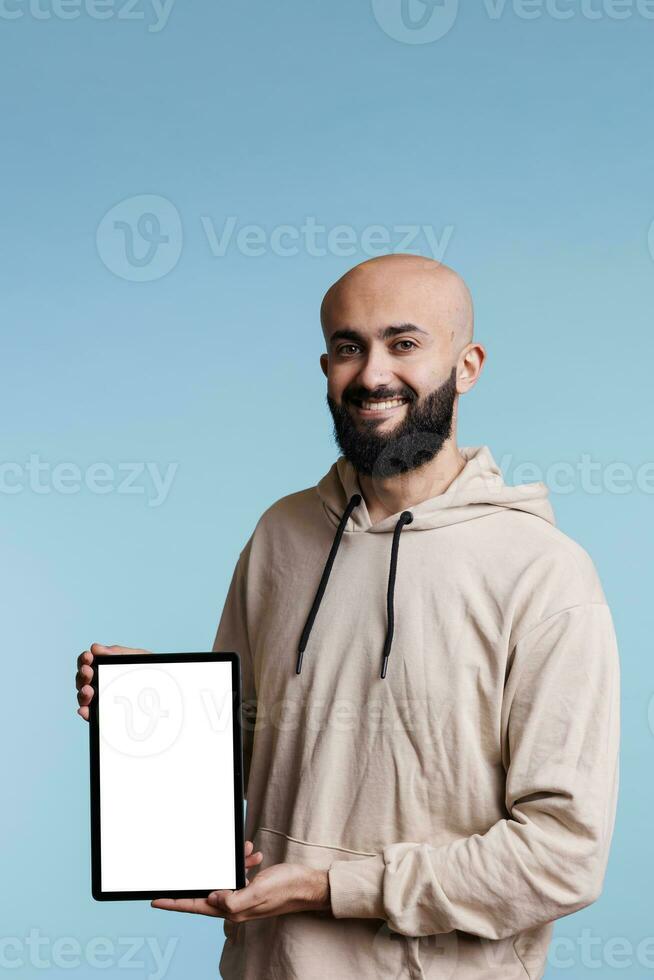 Smiling cheerful arab man holding digital tablet with white empty screen portrait. Carefree person showing portable device, displaying mock up for app ads and looking at camera photo