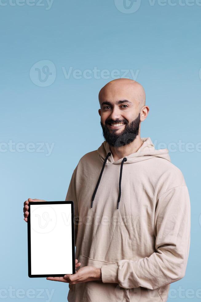 Smiling cheerful arab man holding digital tablet with white empty screen portrait. Carefree person showing portable device, displaying mock up for app ads and looking at camera photo