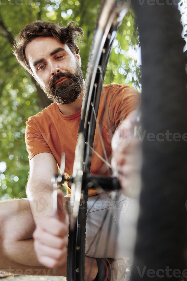 Committed healthy and active man outdoor showing dedication in adjusting and securing bicycle parts for recreational summer cycling. Image showing young man fixing bike wheel, summer activity. photo