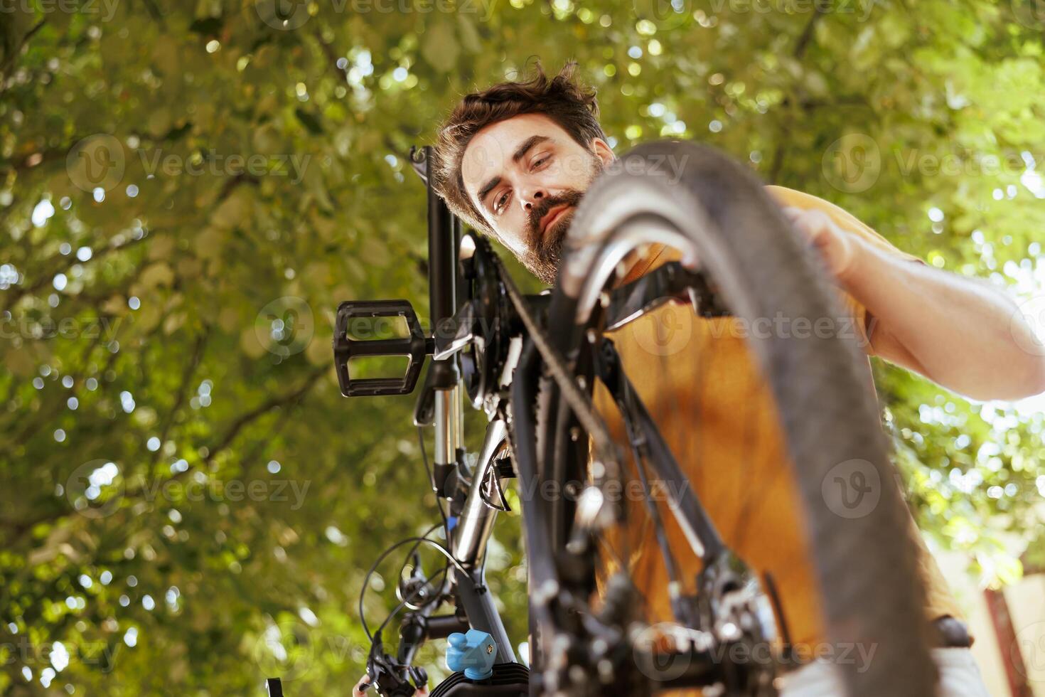 Young committed male cyclist making annual adjustments to pedals and chains outdoor. Active enthusiastic man repairing and maintaining bicycle parts with professional tool. photo