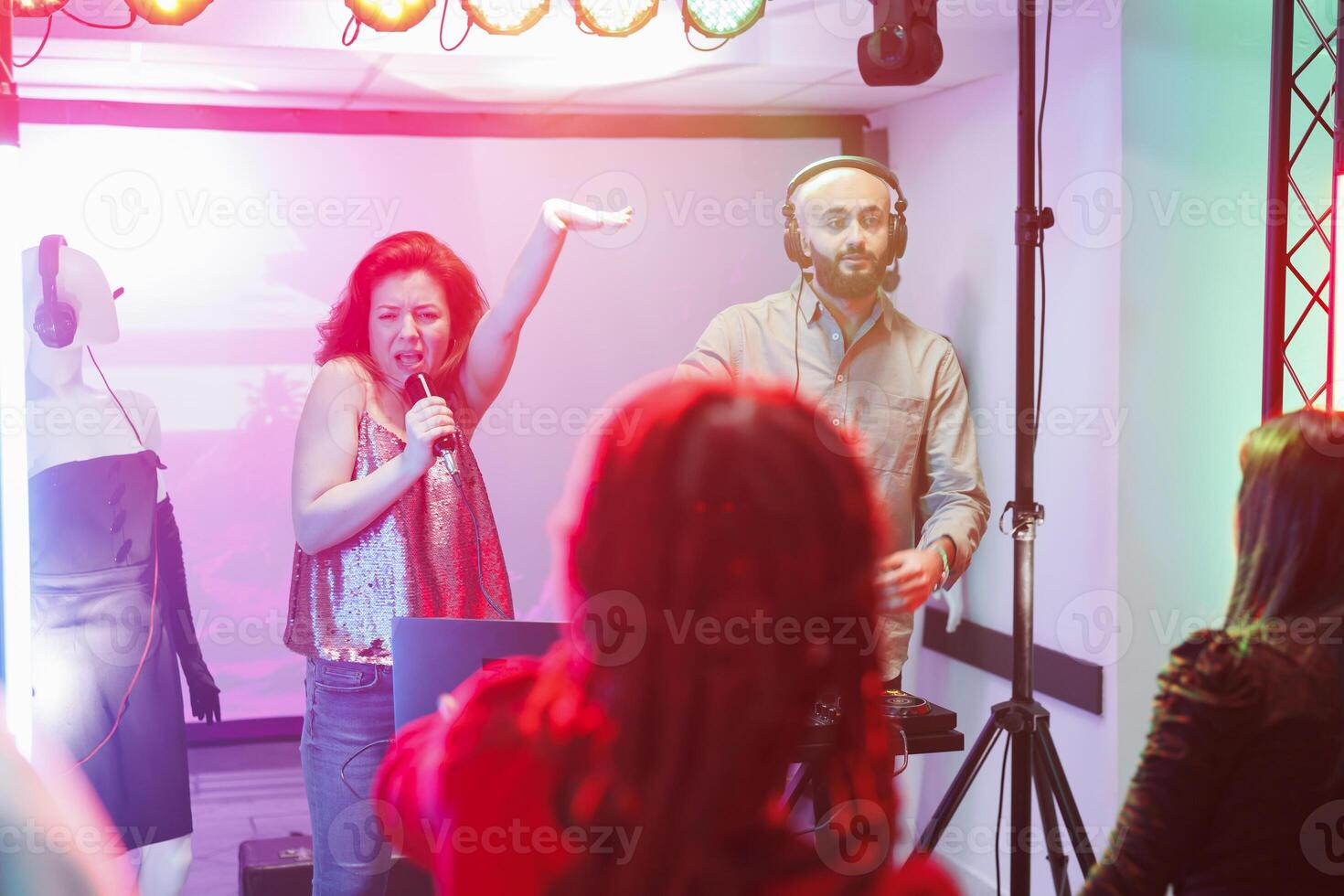 Electronic music band performing on stage with spotlights at concert in nightclub. Woman singing and man dj mixing tracks while clubbers crowd dancing and enjoying show in club photo