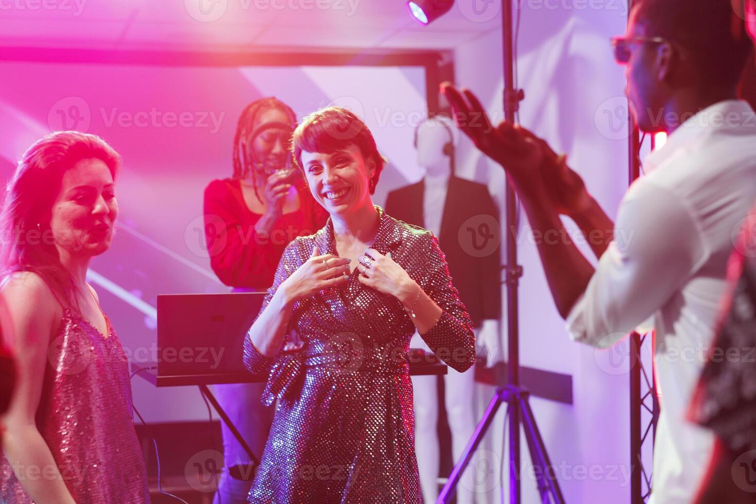 Cheerful woman laughing and looking at camera while dancing with friends at nightclub discotheque. Smiling happy girl having fun on dancefloor in club with spotlights portrait photo
