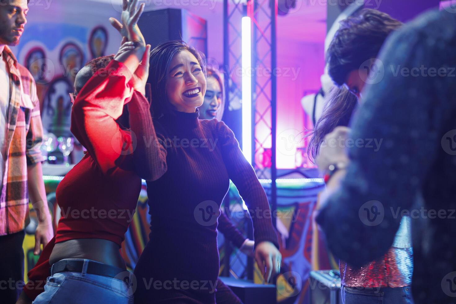 Cheerful smiling diverse women dancing together and laughing while partying and enjoying nightlife in club. Happy girlfriends having fun and celebrating on dancefloor in nightclub photo