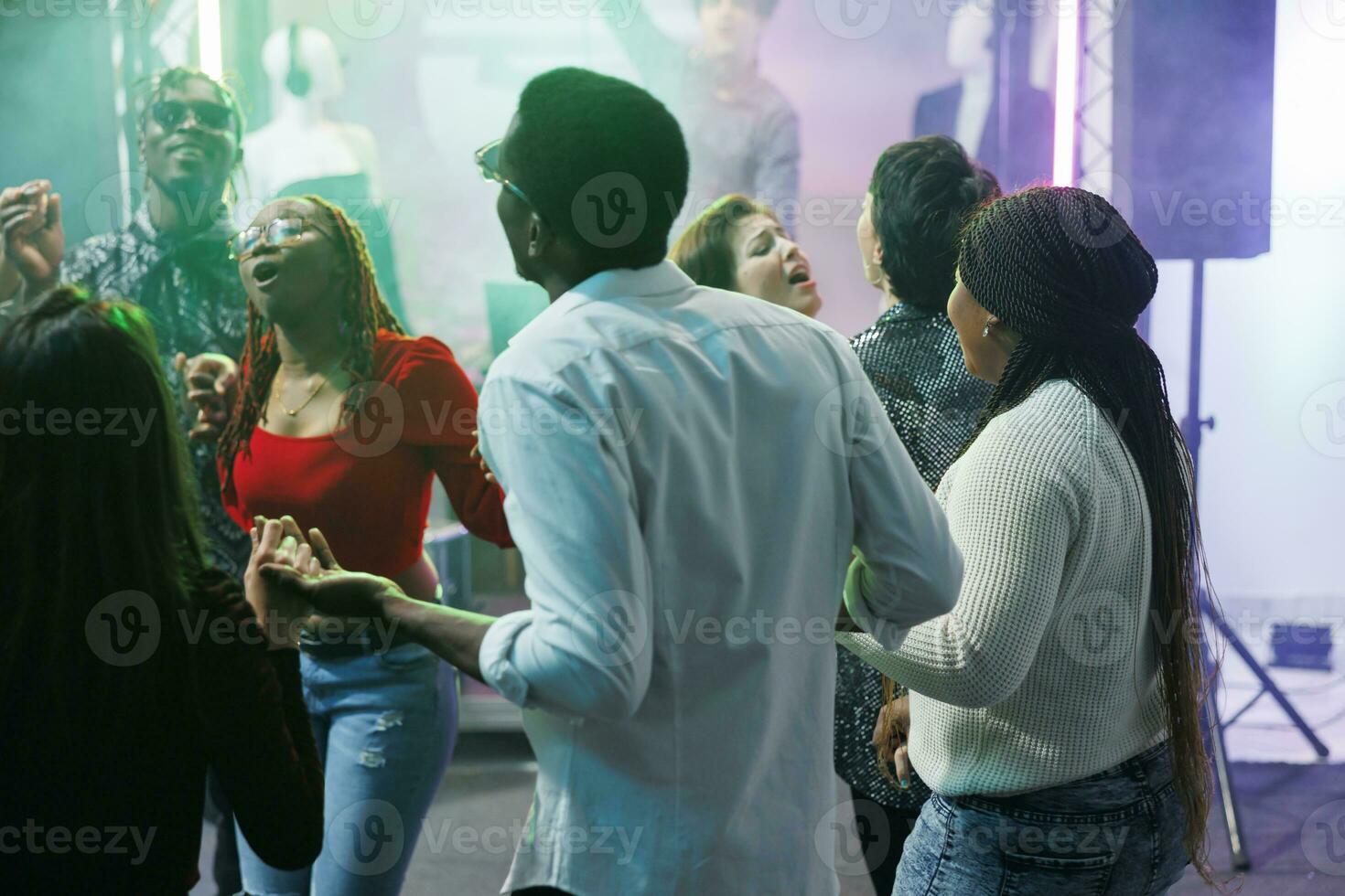 Diverse people clubbing and dancing together at discotheque party event in nightclub. Young friends holding hands, singing and relaxing on crowded dancefloor at social gathering photo