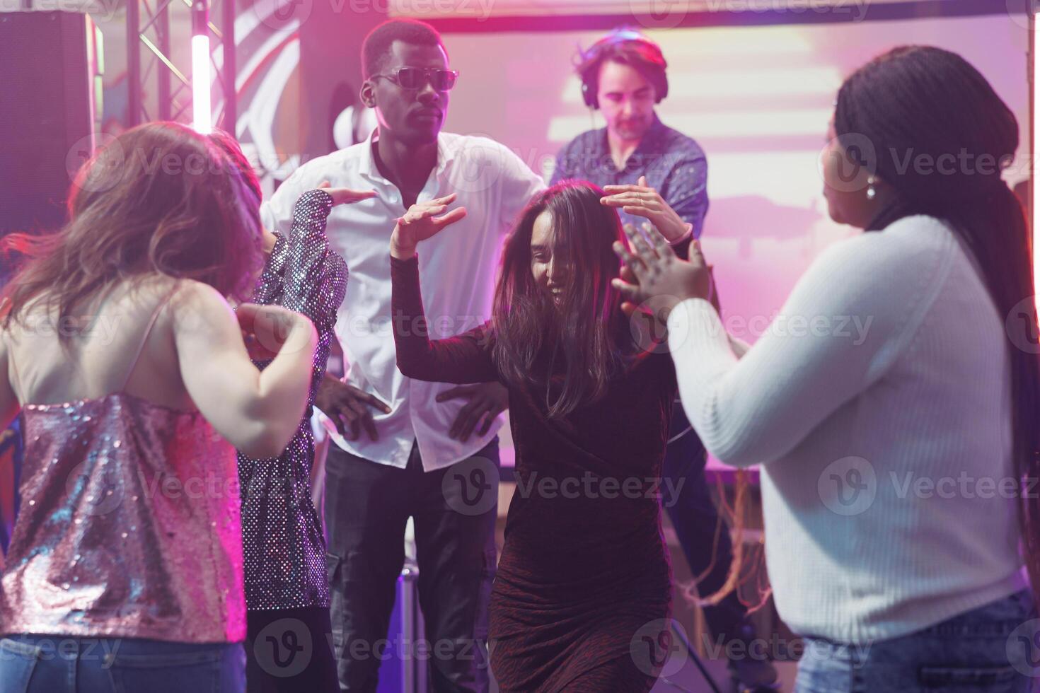 Carefree clubbers friends dancing and having fun together in nightclub. Diverse people making energetic moves to music rhythm on dancefloor at club disco social gathering photo