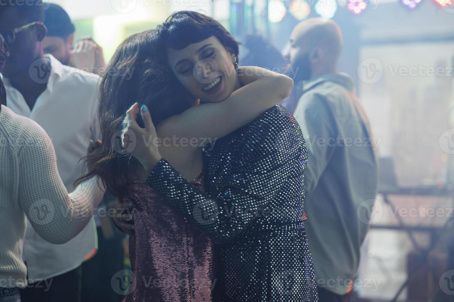 Young women hugging and dancing while attending disco party in nightclub. Romantic girlfriends couple embracing on dancefloor while clubbing and relaxing at discotheque event in club photo