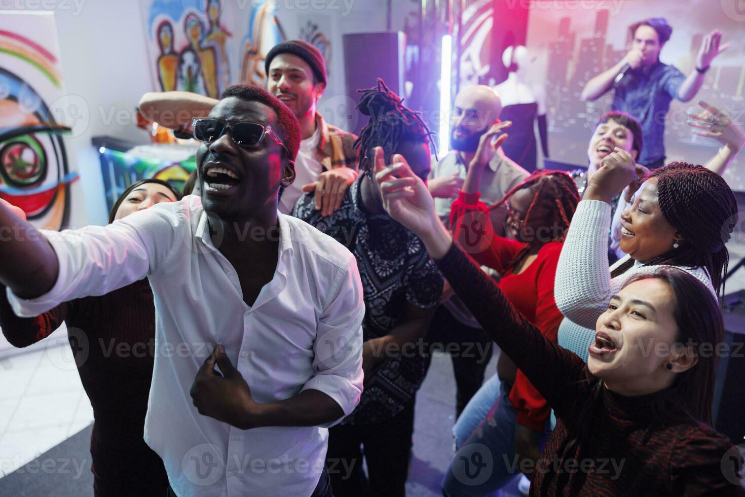 Happy friends group posing for selfie together while having fun and relaxing at nightclub party. Cheerful young diverse people crowd screaming and laughing while taking photo on dancefloor