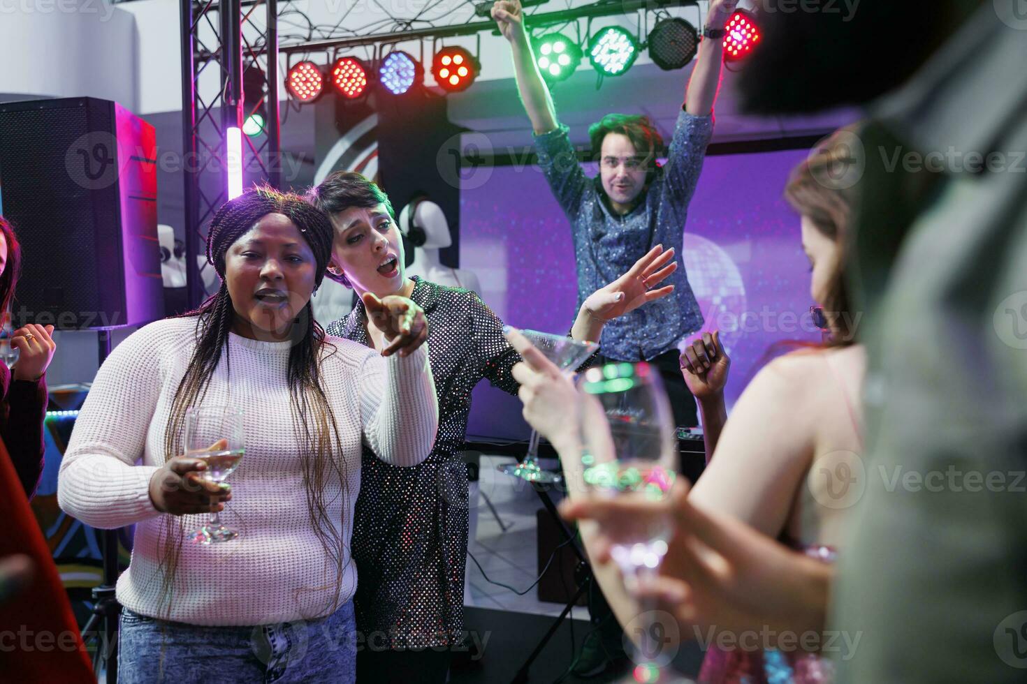 People drinking alcohol, dancing and singing at nightclub party with live music. Cheerful crowd relaxing, enjoying beverages and having fun on dancefloor at social gathering in club photo