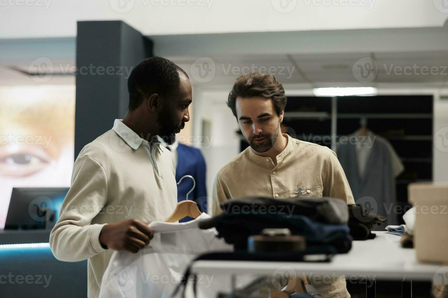 Fashion boutique employee assisting african american customer in choosing formal outfit. Clothing store client getting help from showroom worker while selecting shirt size photo