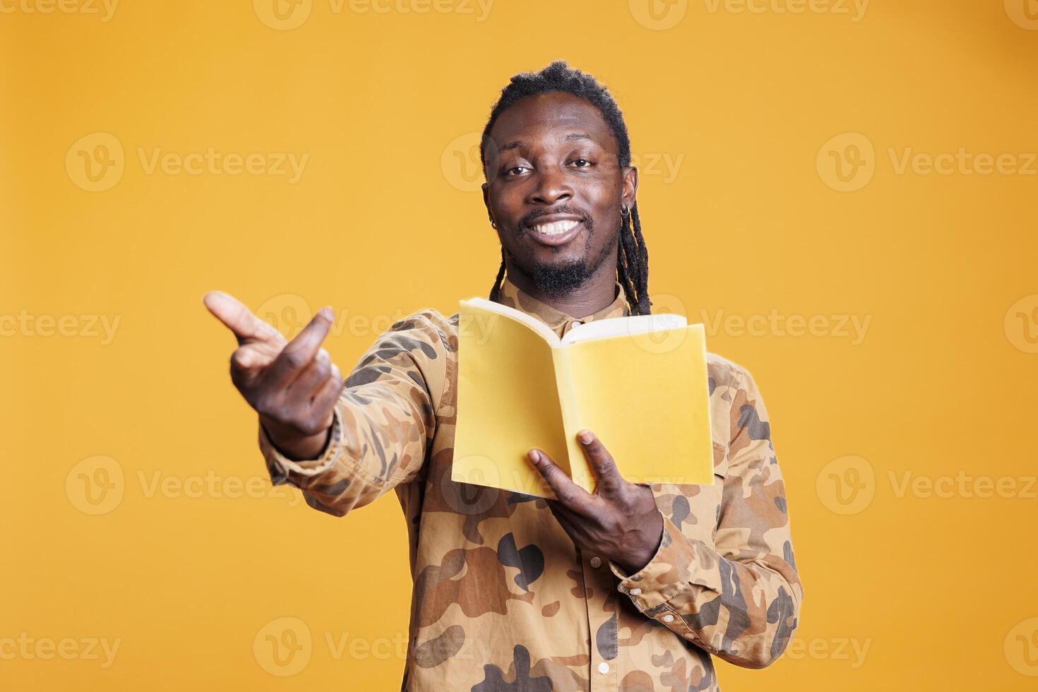 Portrait of cheerful reader being focused on fictional tale during free time, enjoying reading literature book in studio over yellow background. Intellectual man studying for university homework photo