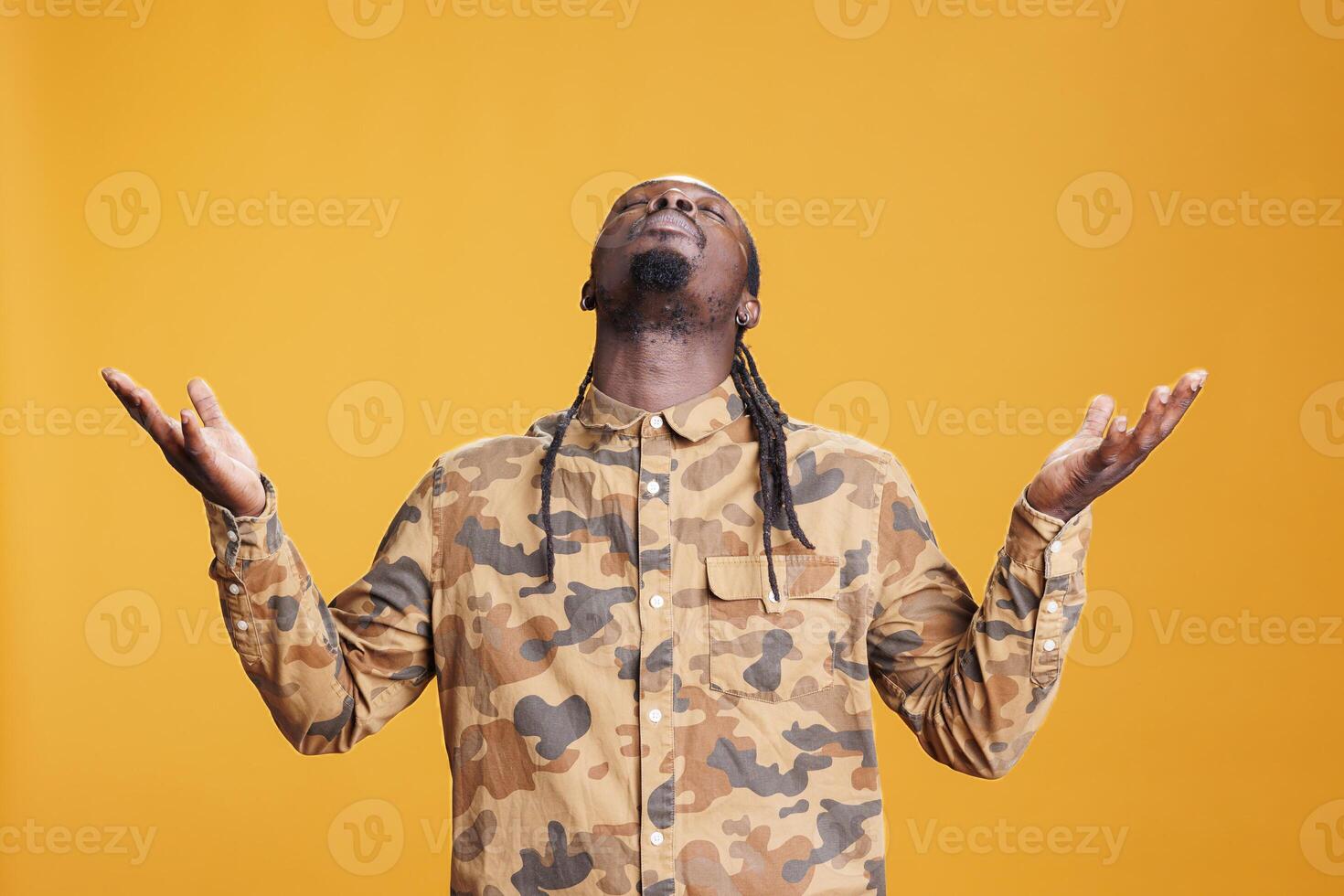 African american prayer standing with palms faced to sky, asking god for forgiveness in studio over yellow background. African american religious man showing gratitude, praying to jesus photo