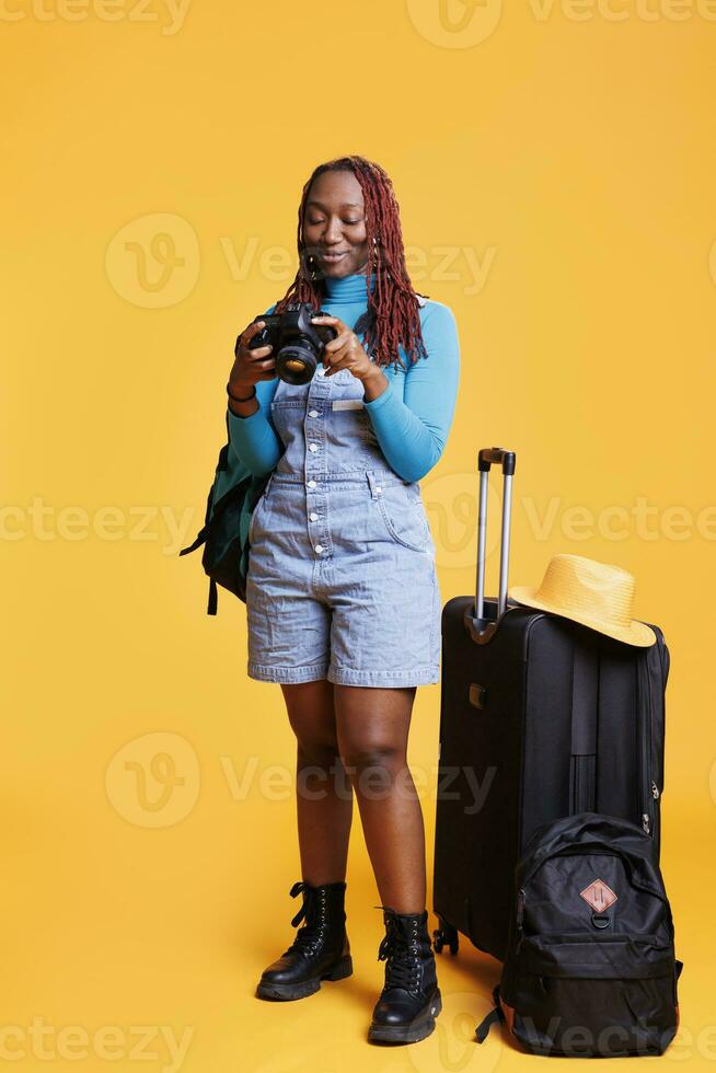 africano americano niña con dslr cámara tomando fotos de edificios arquitectura y escénico ruta. turista capturar imágenes de paisajes y puntos de referencia con carretilla pantalones y maletas