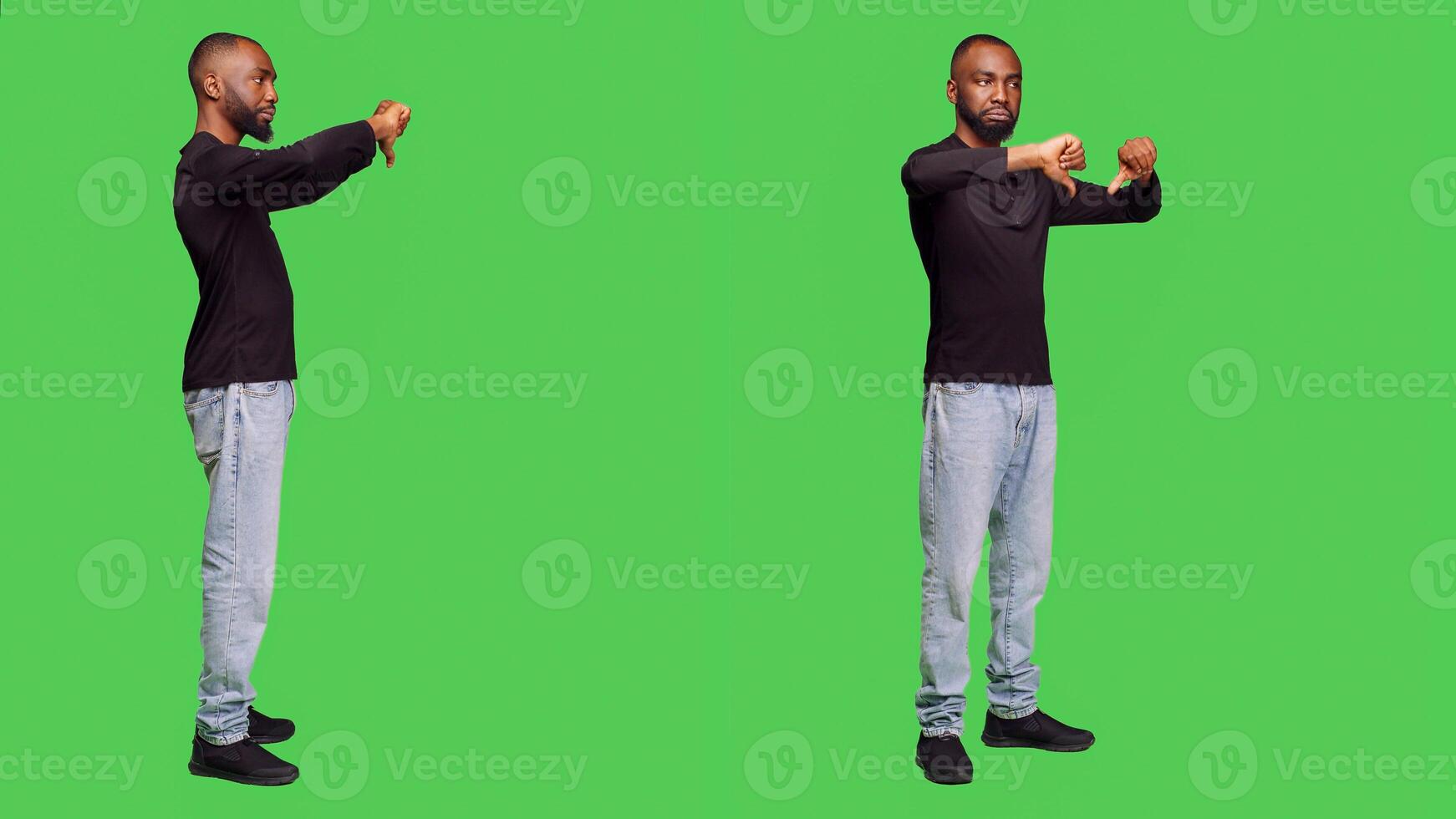 Displeased man showing thumbs down gesture on camera, doing disagreement and disapproval sign in studio. Casual adult posing over full body green screen background, dislike negative symbol. photo