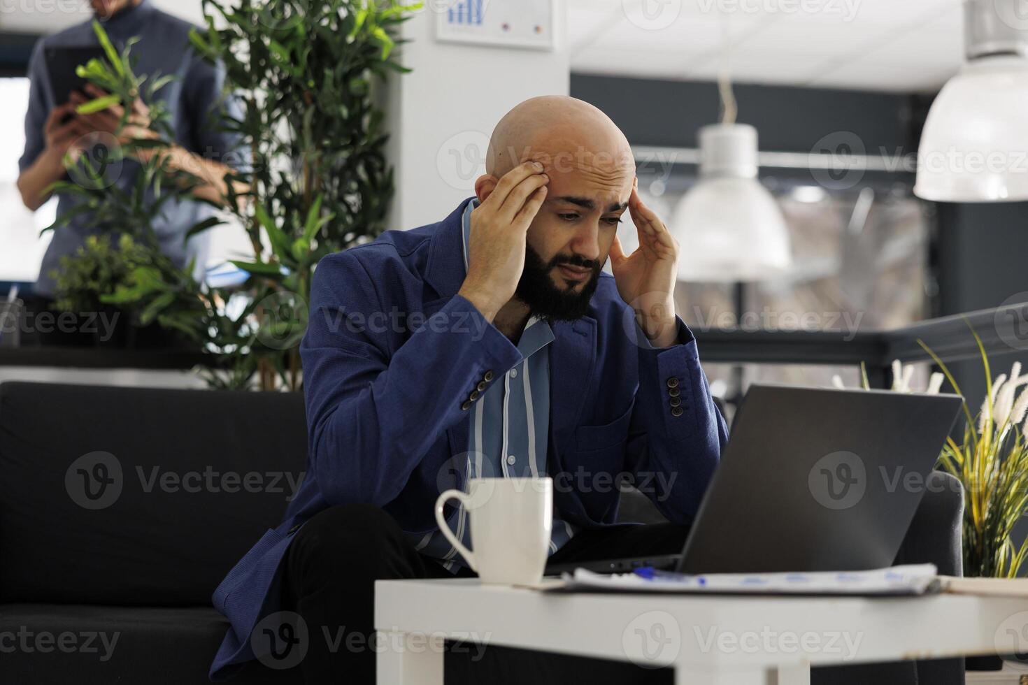 Arab entrepreneur suffering from migraine while working at presentation on laptop. Young company executive manager with headache planning marketing strategy in coworking space photo