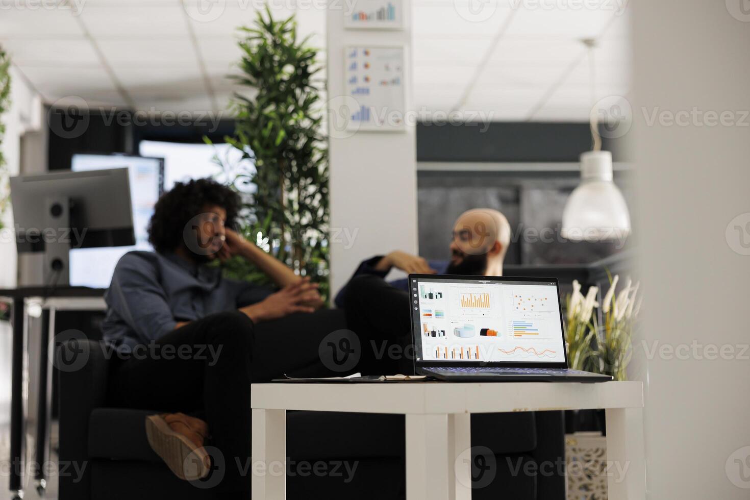 Stock market investment revenue statistics report on laptop screen in office. Arab business company employees sitting on couch in coworking space and discussing financial analytics photo