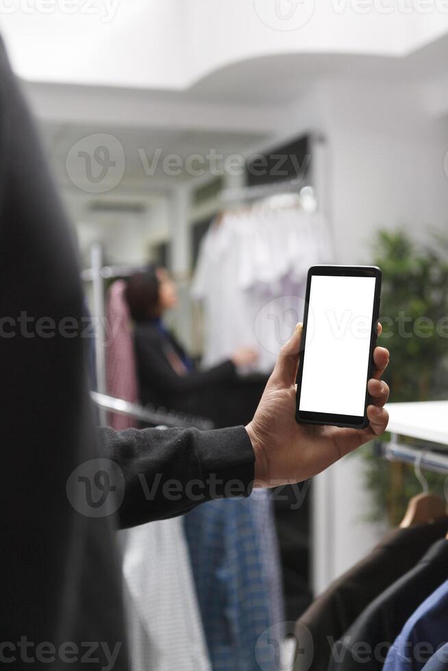 Customer in retail store using mobile phone empty white digital display while checking available apparel options. Shopping mall boutique client showing smartphone blank touchscreen photo
