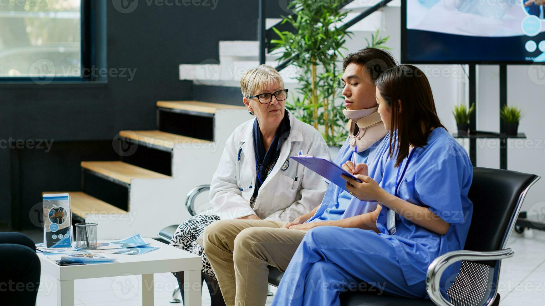 médico que se discute con lesionado paciente a eliminar cuello collar durante examen en esperando área. asiático asistente participación portapapeles escritura médico pericia, planificación salud cuidado tratamiento foto