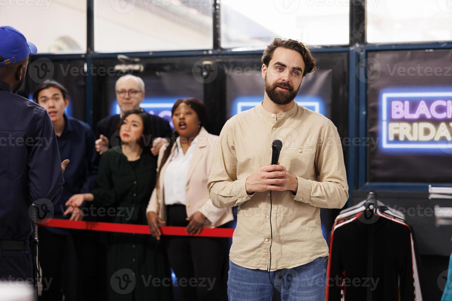 Male television reporter standing in crowded clothing store holding microphone producing live newscast about Black Friday madness. Retail store owner launching start of seasonal sales photo