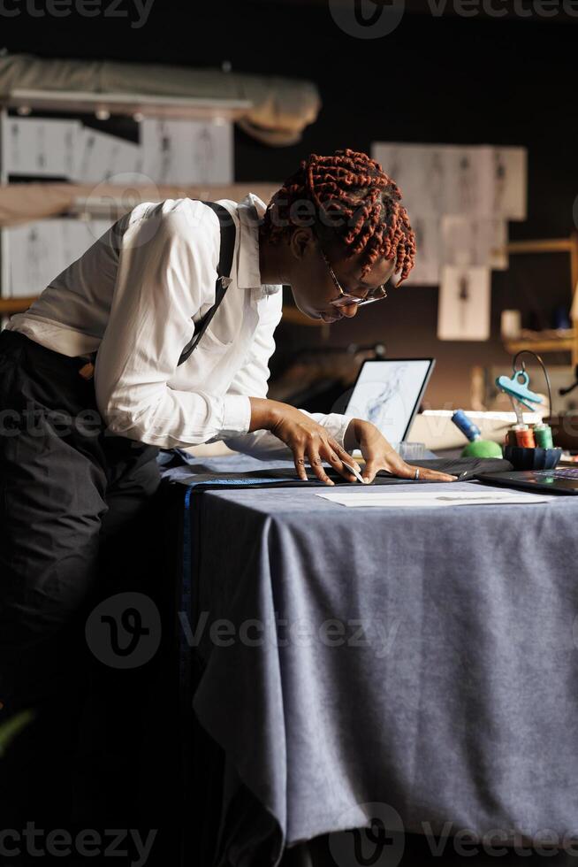 Precise seamstress meticulously doing seam measurements on fancy suit blazer using tape. Skilled seamstress in tailoring studio checking bespoken sartorial stylish garment fits customer photo