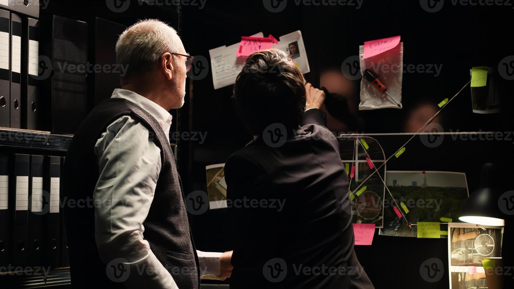 Police agents examine evidence board in investigation office, analyzing unearthed clues to build case file. Detectives team working with classified documents and records to catch suspect. photo