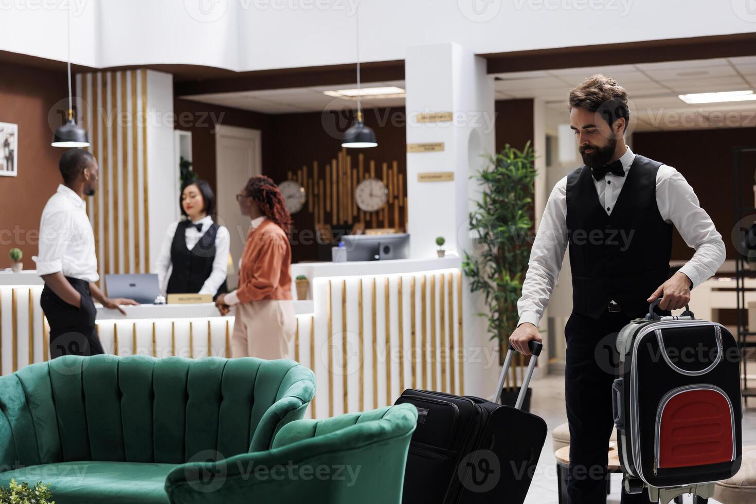 Hotel bellboy carrying bags for guests, helping tourists to find room after doing check in procedure. Male employee acting as concierge, providing luxury service for people with luggage. photo