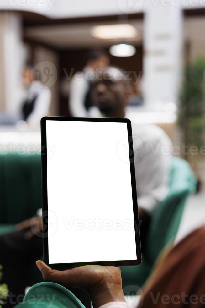 Female person looking at white screen on digital tablet, using blank display with copyspace in lounge area at hotel lobby. Young adult holding device with isolated template. Close up. photo