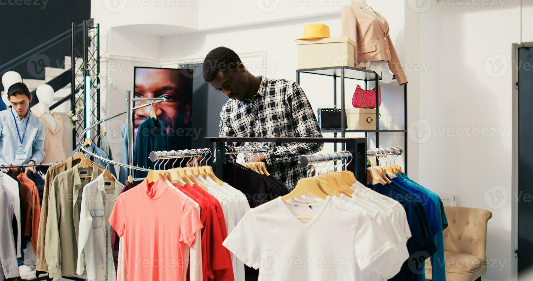 African american man checking rack with new fashion collection, analyzing merchandise material in clothing store. Shopaholic client shopping for fashionable clothes in modern boutique photo