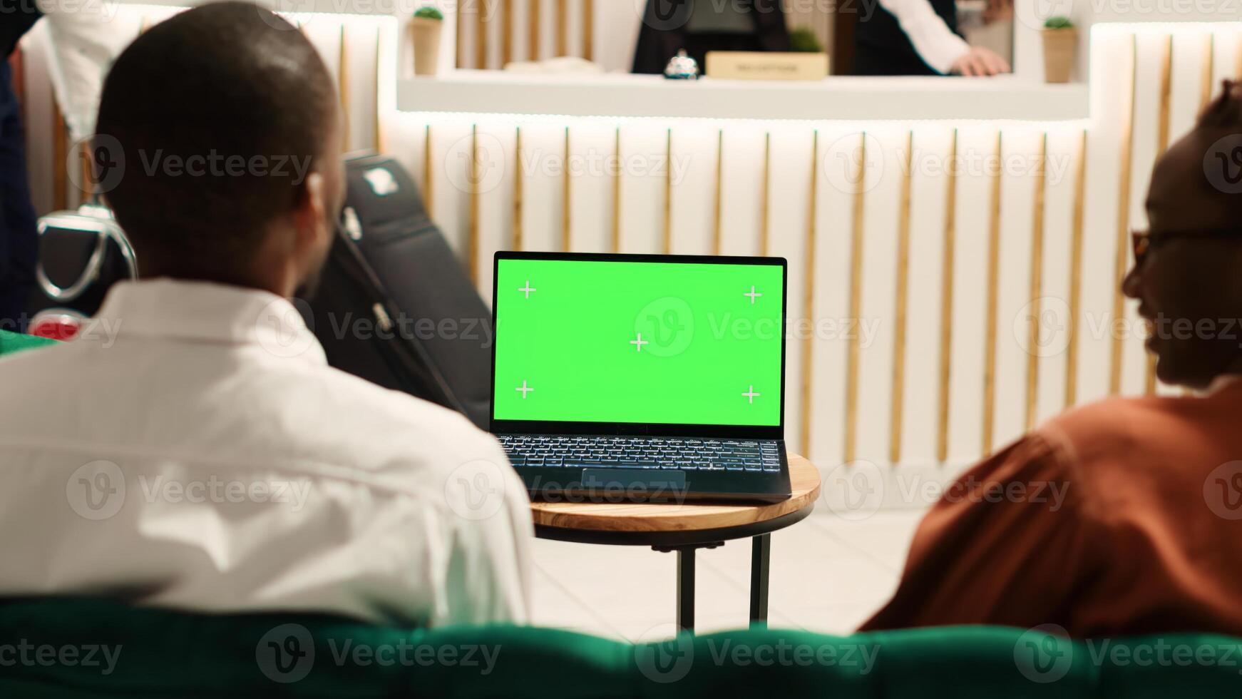 Happy african american tourists watching video on laptop chroma key green screen mock up while sitting in hotel foyer. Guests waiting to be checked in, streaming movie in resort lounge photo