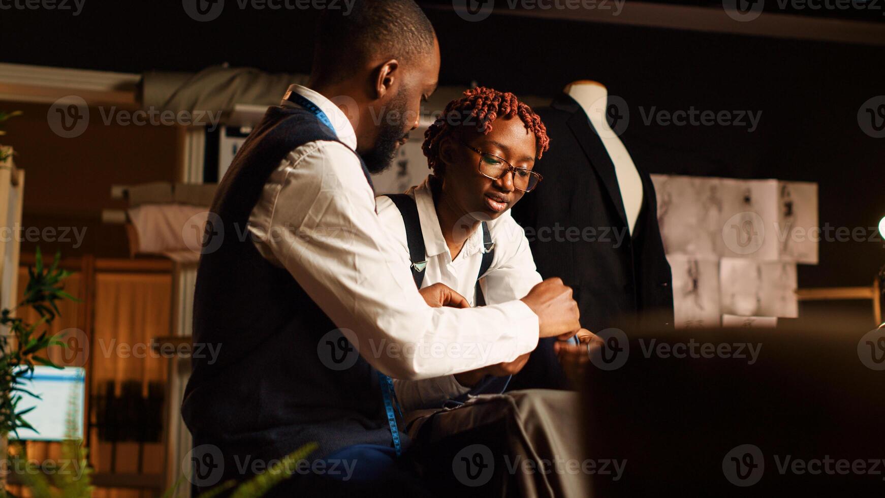 Designers reviewing material for items in atelier, choosing professional fabric on workstation before creating clothing line. Team of tailors manufacturing clothes with tools. Handheld shot. photo