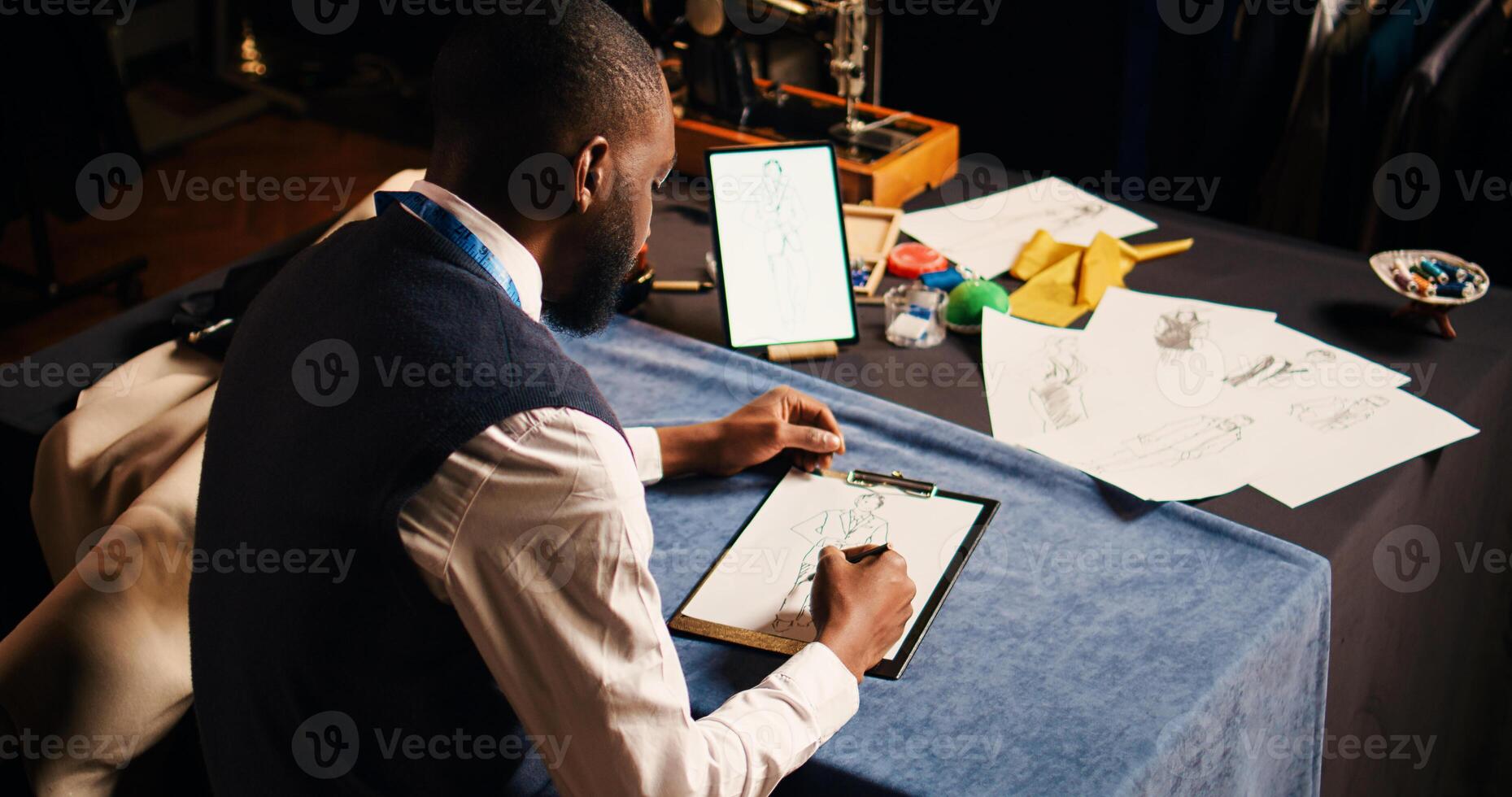 Male couturier drawing outlines of clothes, creating models for clothing items design at workstation. Young business owner working as tailor, manufacturing custom made clothes. photo