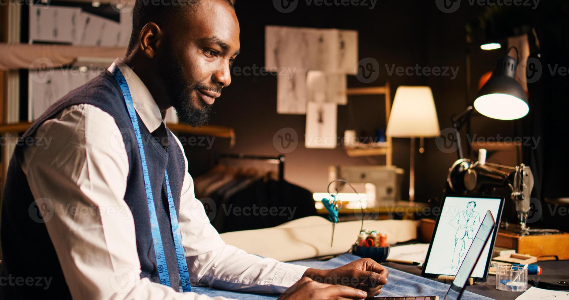 Young fashion designer using laptop in crafting atelier, searching for clothes design inspiration and models. Professional tailor business owner preparing for handcraft process. photo