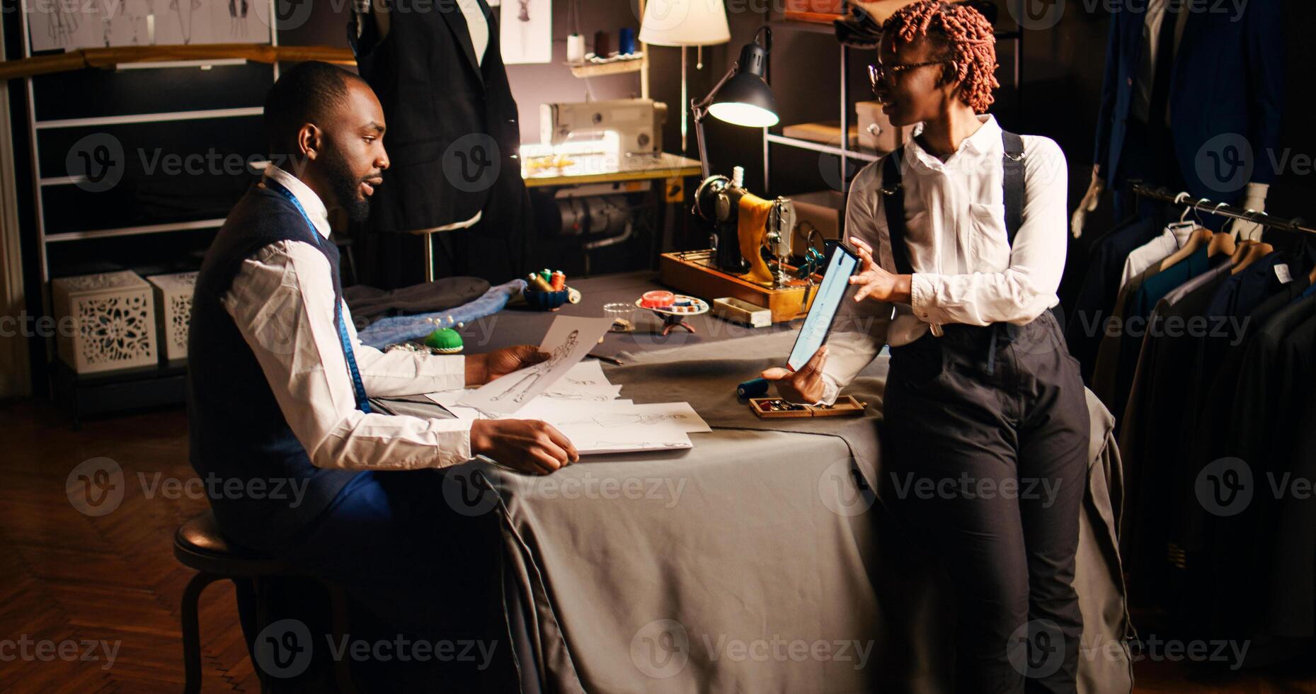 Tailors choosing design of clothes using modern fashion sketches in atelier, discussing about fabric and sewing type. Team of couturiers working on designing tailored clothing line. Handheld shot. photo