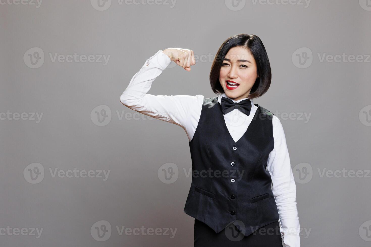 Attractive asian waitress showing bicep strength concept and looking at camera. Young strong