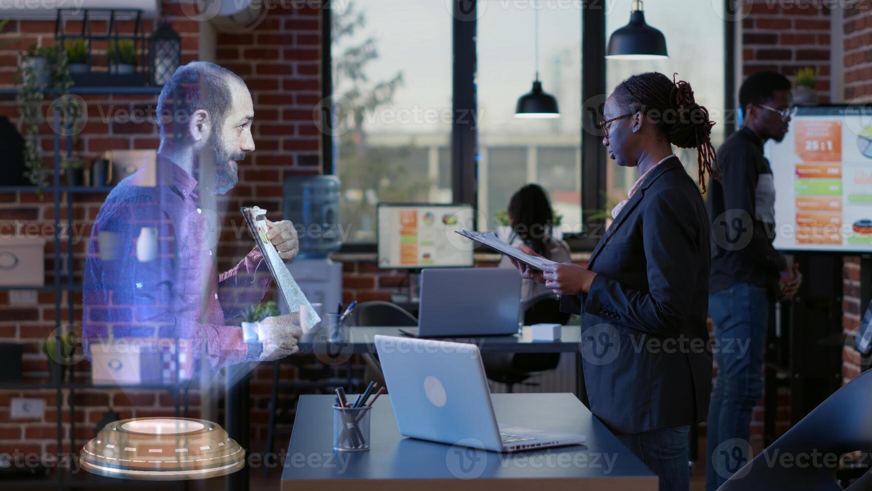 Team leader AR teleconference meeting in modern office talking with african american employee. Businesswoman at workspace desk in online holographic videocall with management executive photo