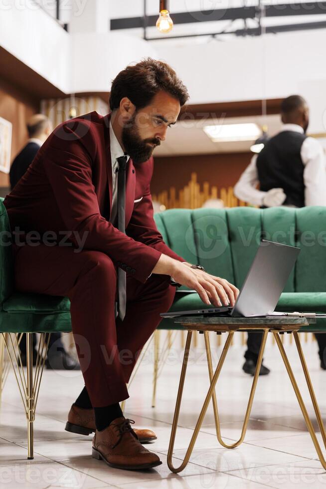 Entrepreneur reads papers in hotel lobby, waiting for check in registration before attending official conference. Businessman reviewing presentation notes for corporate meeting abroad. photo