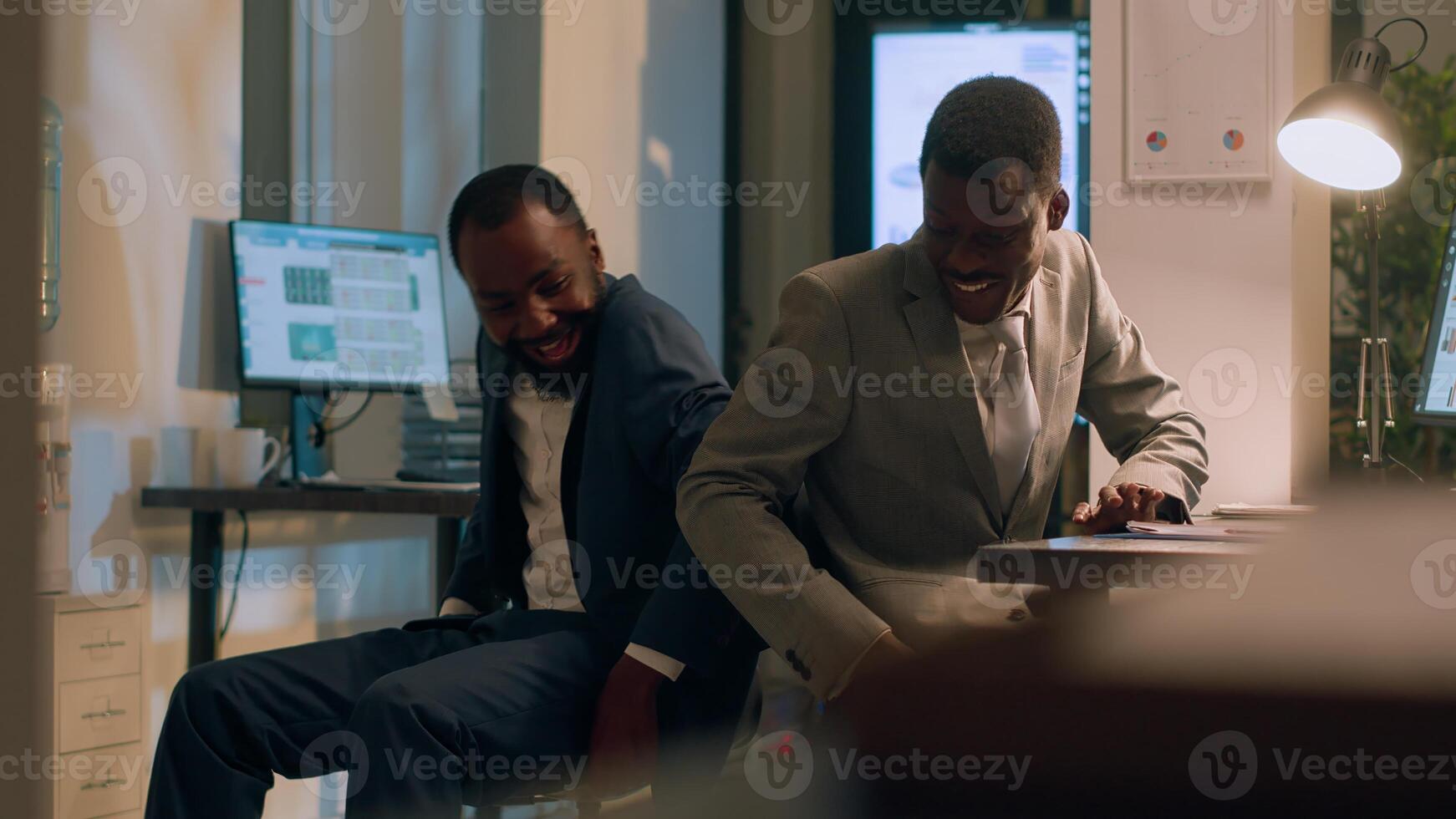 Funny worker distracting colleague during nightshift, bumping into him using desk chair. Happy coworkers racing eachother to avoid tediousness during overnight stay in office photo